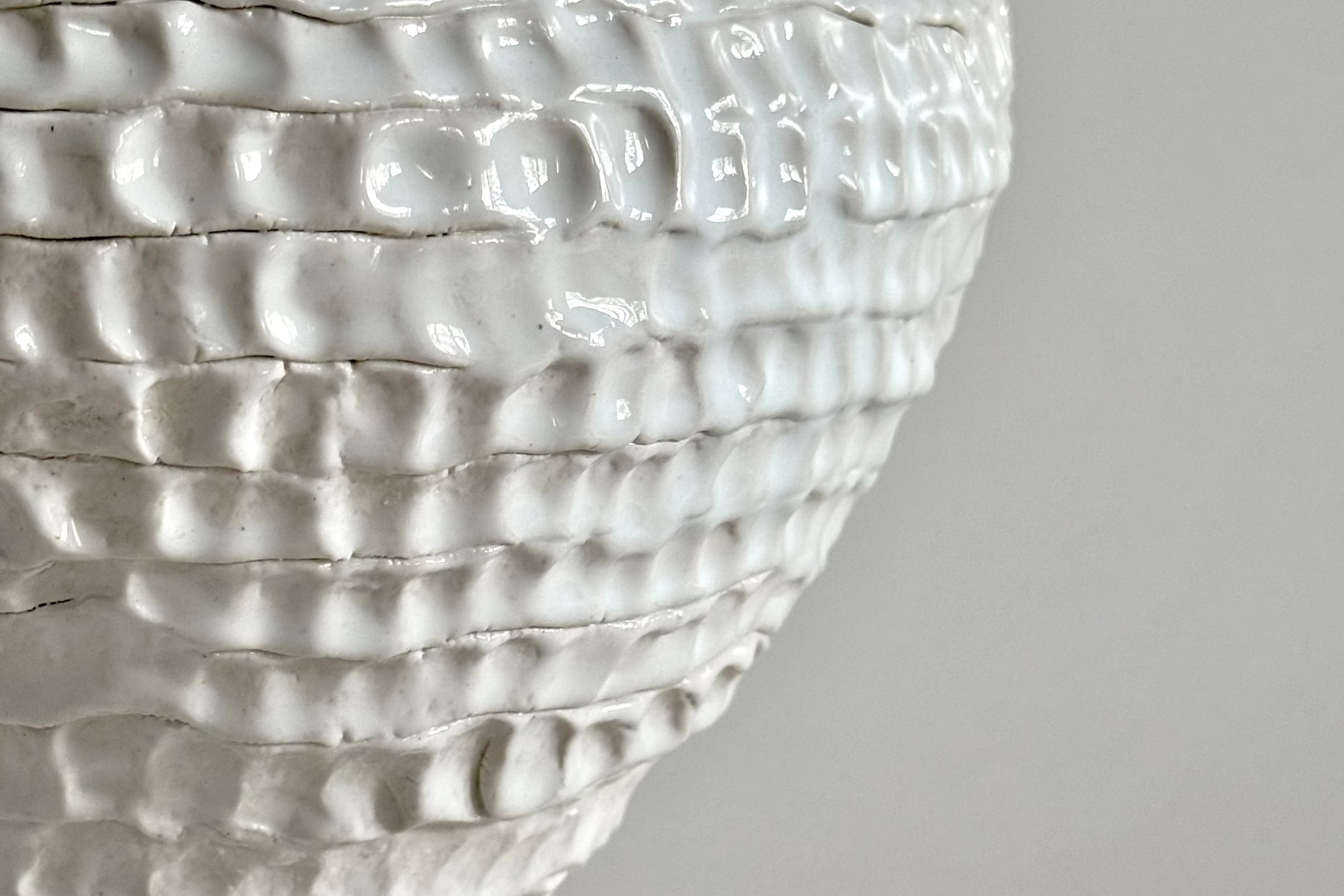 Close-up of a glossy white textured ceramic vessel, showing its ribbed, organic surface detail against a neutral light gray background.